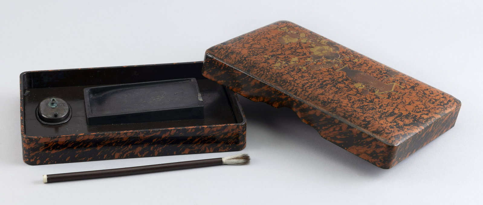 JAPANESE GILT, ORANGE AND BLACK LACQUER SUZURIBAKO Meiji Period Height 1.5î. Length 6î.: JAPANESE GILT, ORANGE AND BLACK LACQUER SUZURIBAKO Meiji Period Jardiniere decoration against a faux bois ground. Interior fitted with an inkstone, brush and water dropper. Signed on inside cover. Hei