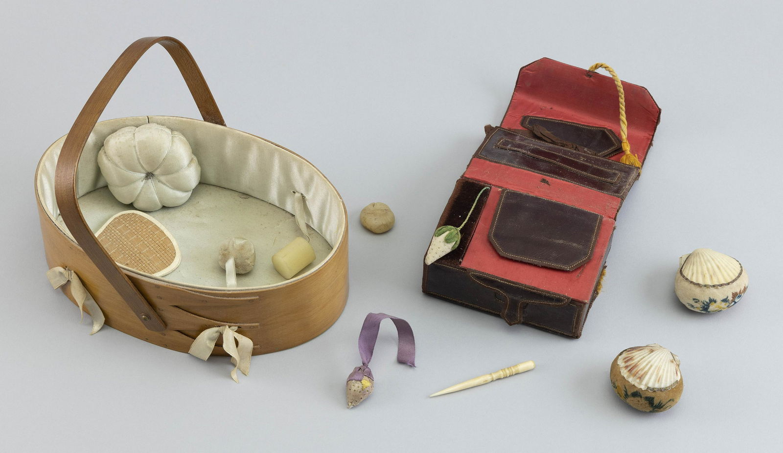 SHAKER SEWING ETUI 19th Century Box length 8î.: SHAKER SEWING ETUI19th CenturyIncludes an oval wooden swing-handled box, two shell-form pincushions, wax and a leather needle case.Box length 8î.