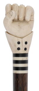 CLENCHED FIST CANE Late 19th Century Length 37".: CLENCHED FIST CANE Late 19th Century Marine ivory handle carved as a clenched left fist and shirt cuff inlaid with ebony buttons and banding. Striated wood shaft inlaid with diamond-shaped abalone