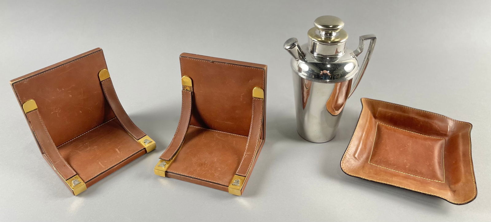 DESK AND BAR ACCESSORIES Last Half of the 20th Century: DESK AND BAR ACCESSORIESLast Half of the 20th Century1) Holland Brothers brown leather valet tray. Stamped on base. 8" x 7".2) Pair of Mark Cross leather bookends with brass lion's-head logo accents.