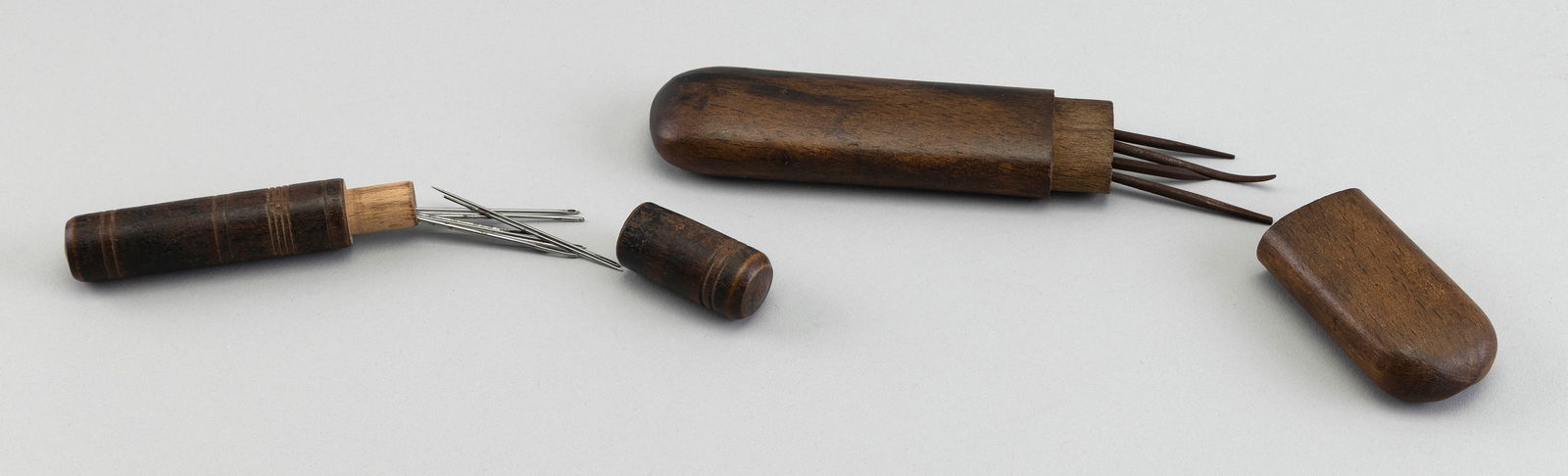 TWO WOODEN NEEDLE CASES 19th Century Lengths 4.5" and 6.75".: TWO WOODEN NEEDLE CASES19th CenturyOne cylindrical with incised banding. Other oblong. Both contain metal needles.Lengths 4.5" and 6.75".