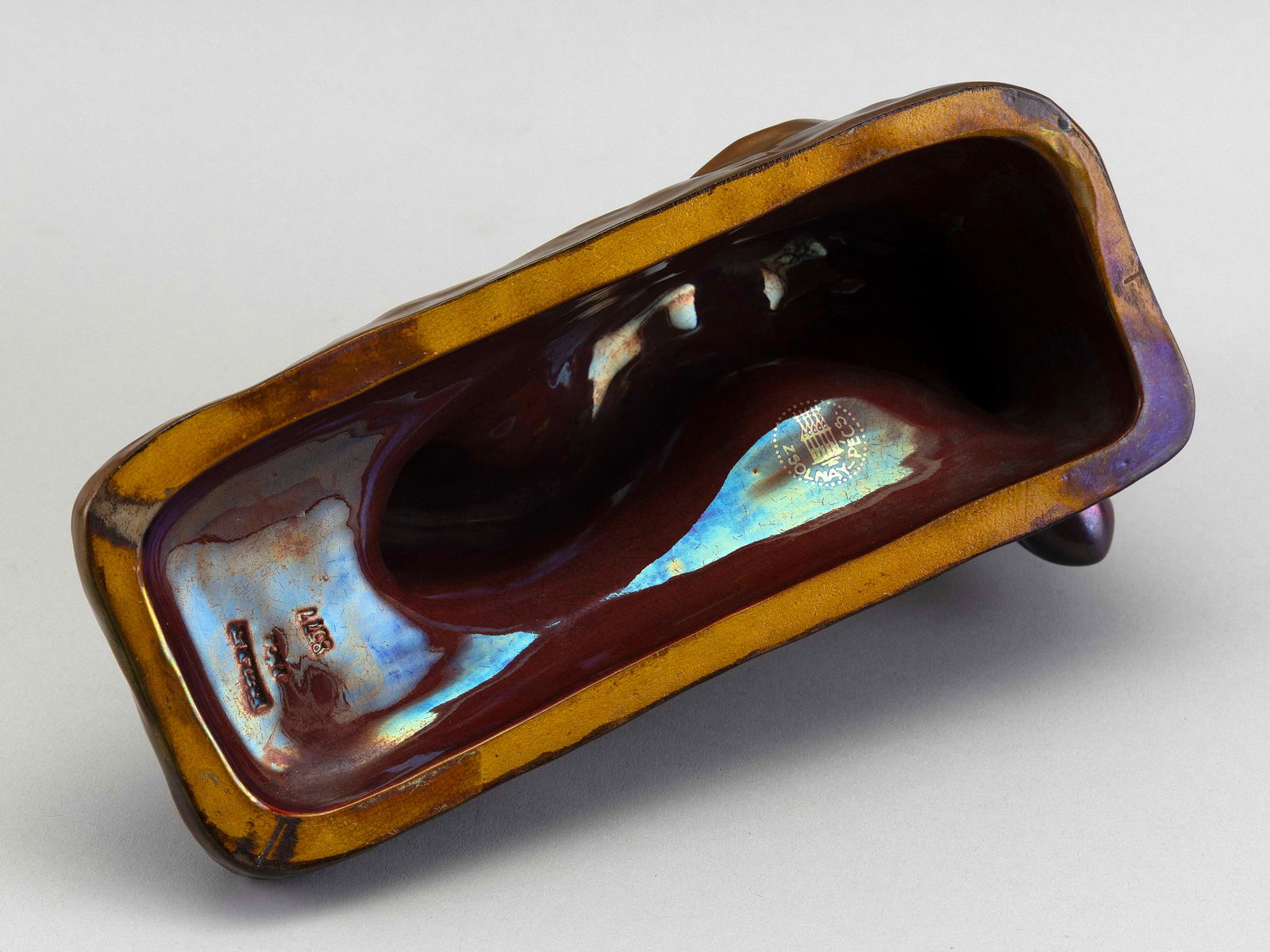 ZSOLNAY PECS PORCELAIN FIGURE OF A RECLINING NUDE WOMAN Hungary, Late 19th Century Height 4.25".: ZSOLNAY PECS PORCELAIN FIGURE OF A RECLINING NUDE WOMANHungary, Late 19th CenturyRed and brown iridescent glaze. Painted and impressed marked. Numbered 8577.Height 4.25". Length 9". Width 4.5".