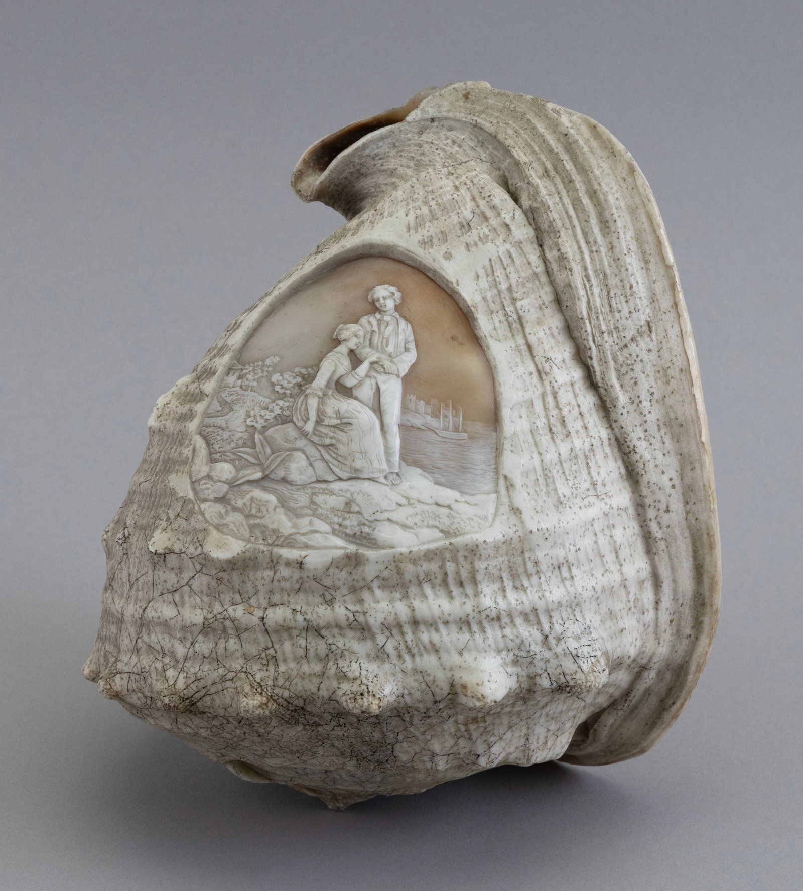 CAMEO CARVED CONCH SHELL DEPICTING A SAILOR'S FAREWELL Mid-19th Century Maximum length approx. 7.5".: CAMEO CARVED CONCH SHELL DEPICTING A SAILOR'S FAREWELL Mid-19th Century Highly detailed coastal landscape with a woman seated on a rock, lovingly resting her hand on the standing sailor's forearm. App