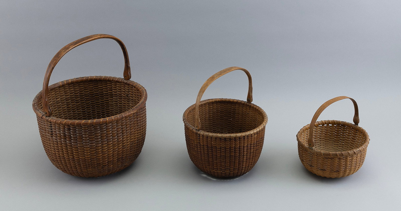 NEST OF THREE NANTUCKET BASKETS Early 20th Century Heights to rim 3.5", 5.5" and 6.5".: NEST OF THREE NANTUCKET BASKETS Early 20th Century Round, with swing handles. Unmarked. Heights to rim 3.5", 5.5" and 6.5".