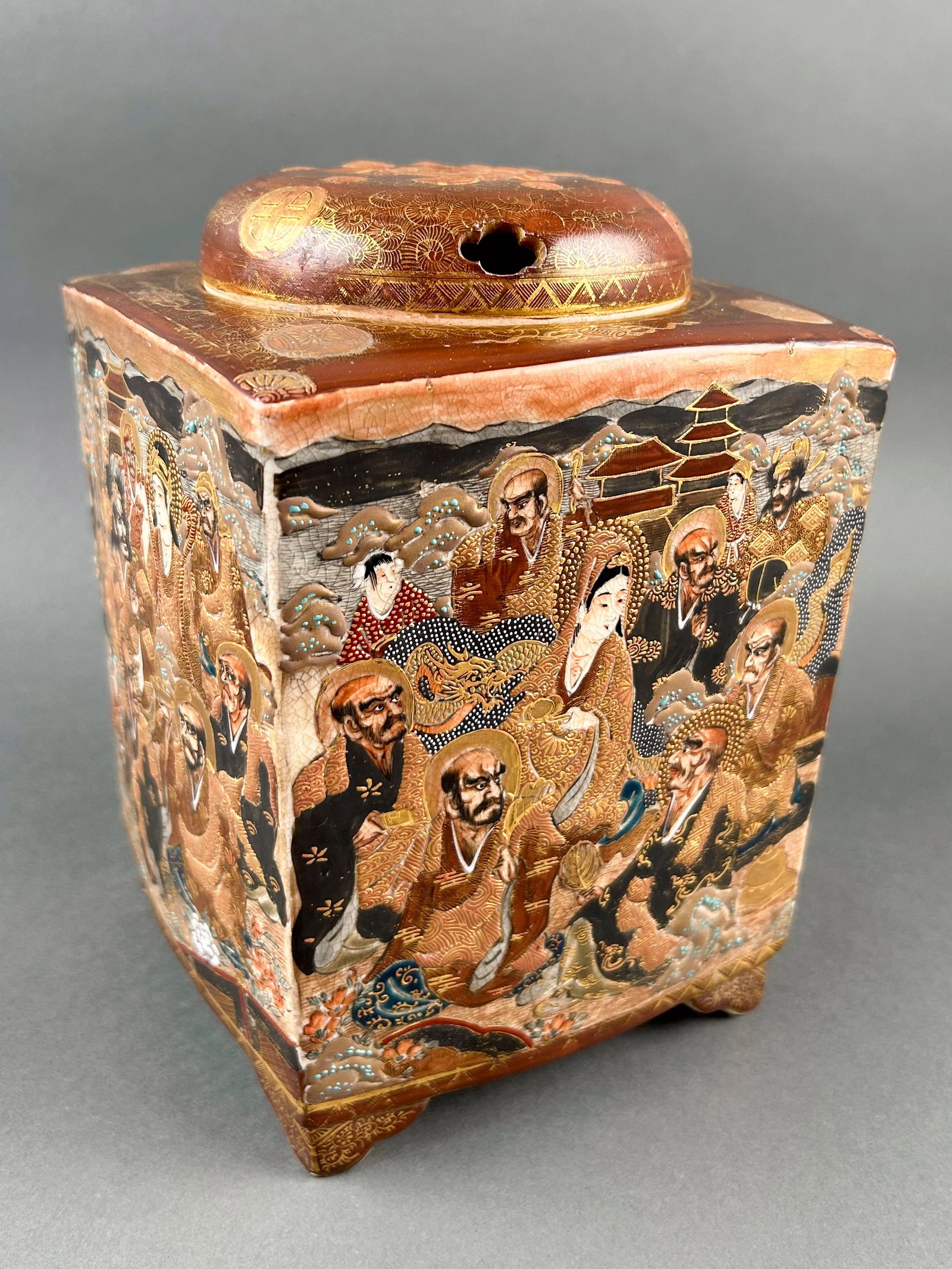 JAPANESE SATSUMA PORCELAIN CENSER Late Meiji Period, Late 19th Century Height 9". Body 6" x 6".: JAPANESE SATSUMA PORCELAIN CENSER Late Meiji Period, Late 19th Century Square body with lohan decoration and four bracket feet. Domed cover with flower and Shimazu mons. Seal marked on base with Shima