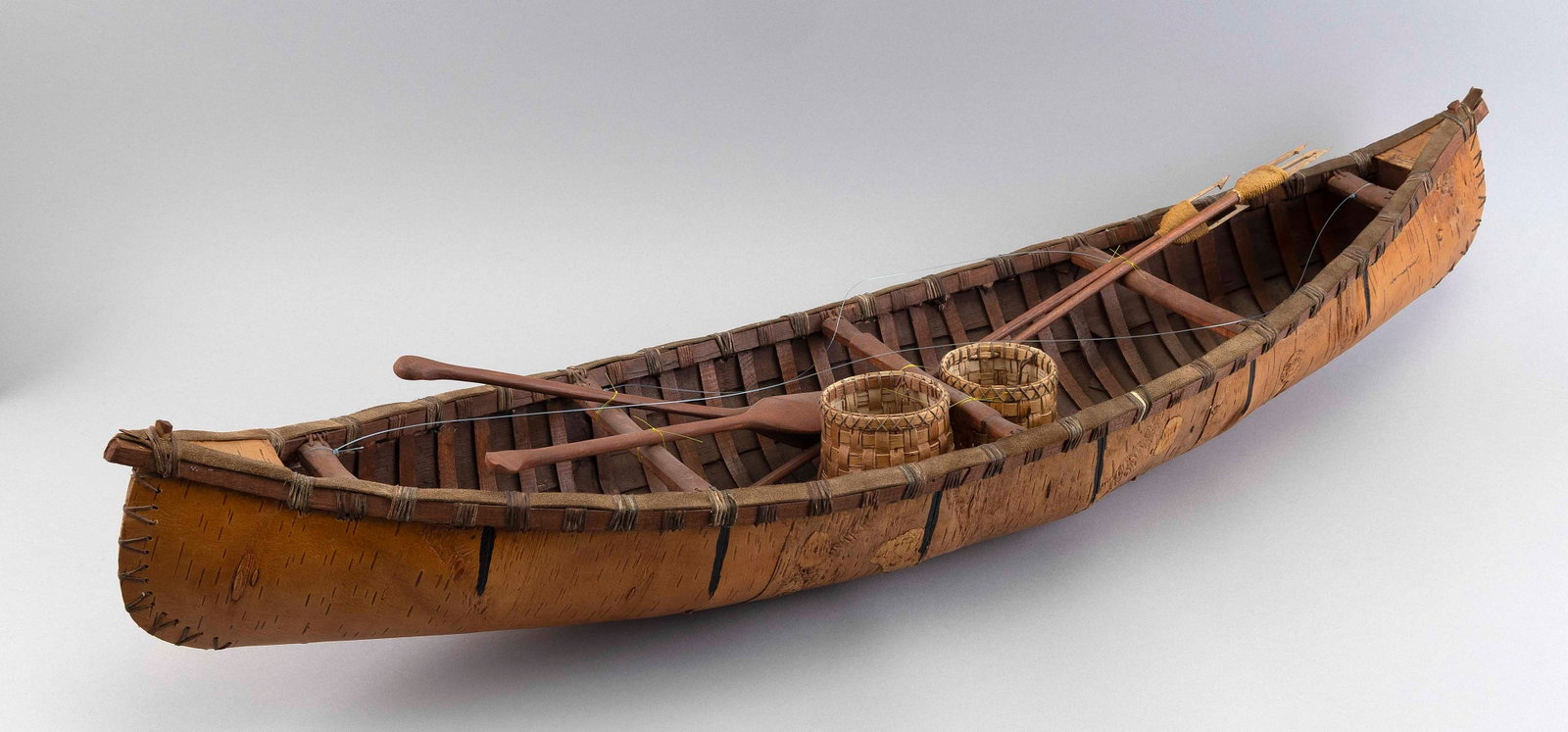 BIRCH BARK CANOE MODEL First Half of the 20th Century Height 7.5". Length 35.25".: BIRCH BARK CANOE MODEL First Half of the 20th Century Wooden ribbed frame. Complete with baskets, spears and paddles. Height 7.5". Length 35.25". Provenance: Private Collection, Wisconsin.