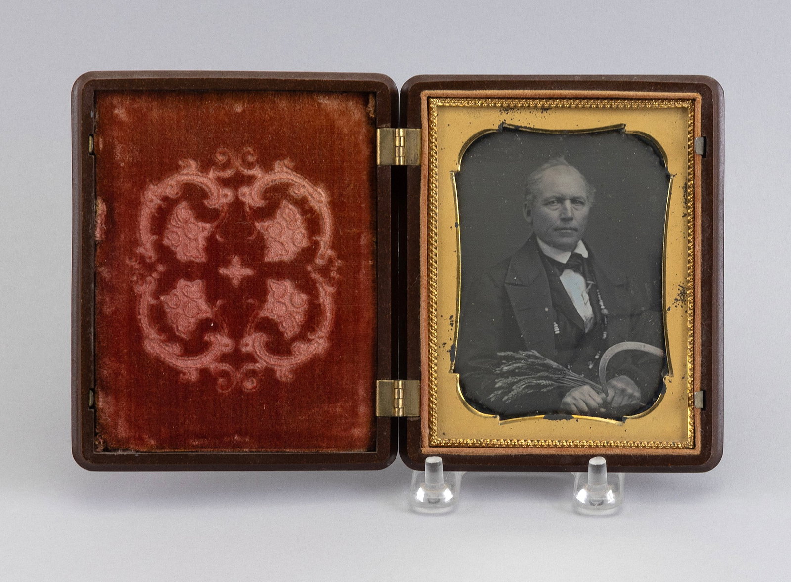 QUARTER-PLATE DAGUERREOTYPE OF A FARMER HOLDING WHEAT AND A SCYTHE 1840s Image 3.75" x 2.75" sight.: QUARTER-PLATE DAGUERREOTYPE OF A FARMER HOLDING WHEAT AND A SCYTHE1840sGreat clarity of image. Housed in a gutta-percha frame with a wheat motif.Image 3.75" x 2.75" sight. Case 4.75" x 4".