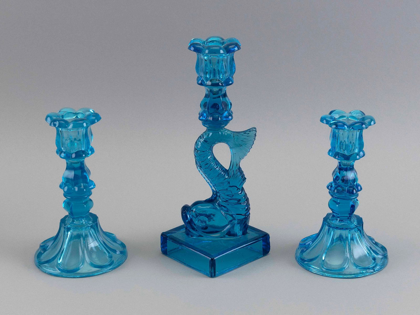 THREE ELECTRIC BLUE SANDWICH GLASS CANDLESTICKS 19th Century Heights from 7" to 10.25".: THREE ELECTRIC BLUE SANDWICH GLASS CANDLESTICKS19th CenturyOne dolphin pattern.Heights from 7" to 10.25".