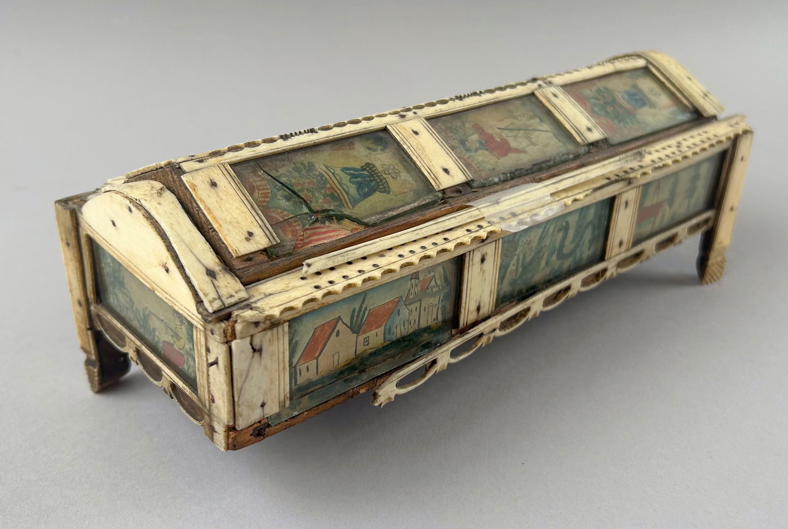 NAPOLEONIC PRISONER-OF-WAR BONE GAMES BOX Britain/France, Early 19th Century Height 3.5". Length: NAPOLEONIC PRISONER-OF-WAR BONE GAMES BOXBritain/France, Early 19th CenturyTriangular sliding cover and perimeter of box with watercolor panels under glass depicting landscapes, portraits, flowering p