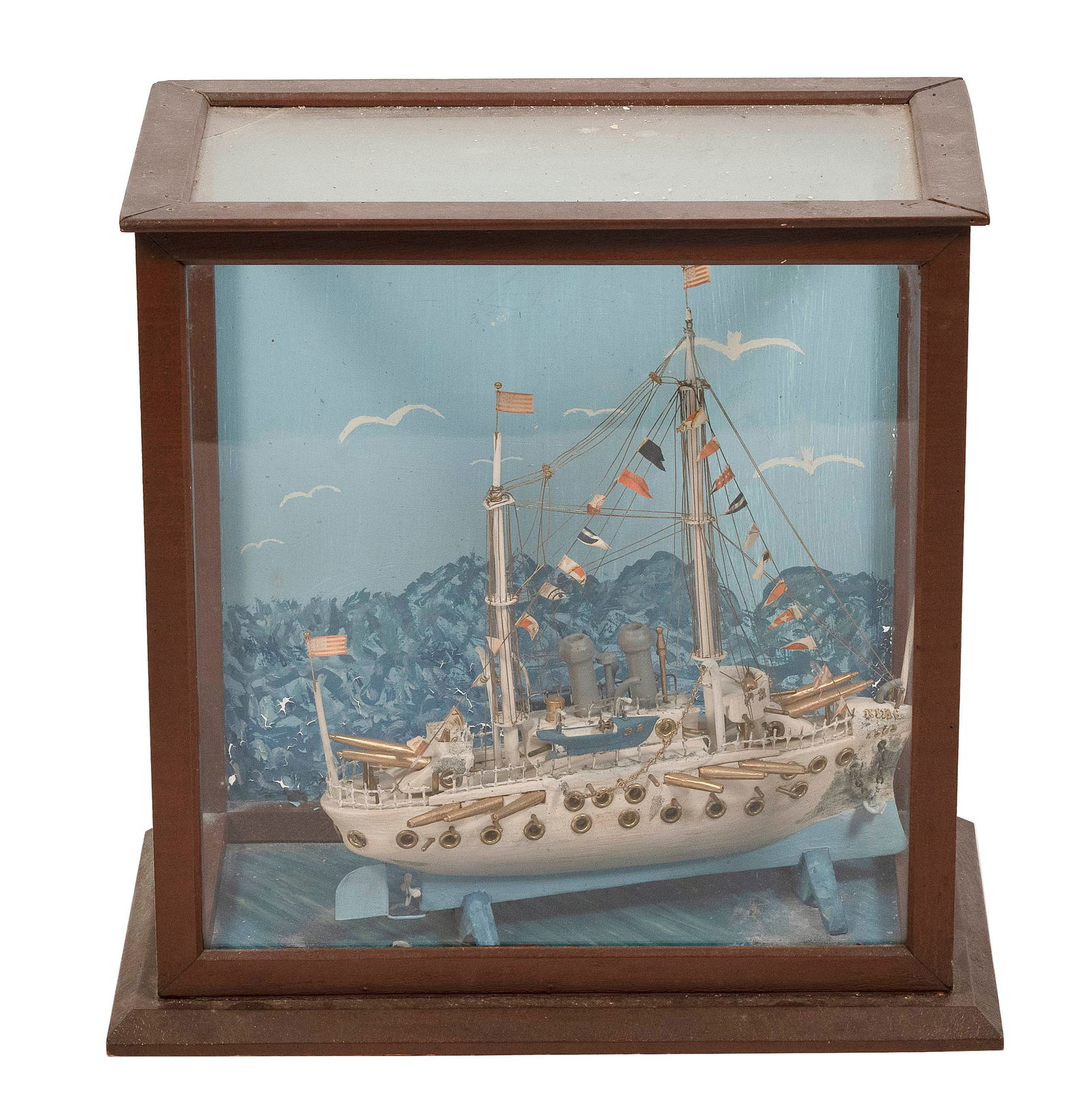 CASED PRIMITIVE MODEL OF A BATTLESHIP Late 19th Century Case height 20". Width 20.5". Depth 12".: CASED PRIMITIVE MODEL OF A BATTLESHIPLate 19th CenturyDisplayed on a cradle within a glass and wood case with painted coastline background.Case height 20". Width 20.5". Depth 12".