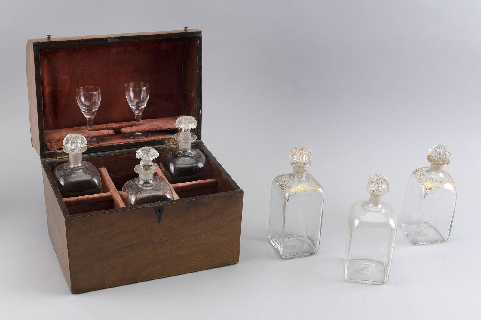 MAHOGANY CAVE A LIQUEUR 19th Century Height 9". Width 10.5". Depth 8".: MAHOGANY CAVE A LIQUEUR19th CenturyFigured mahogany box with half-domed hinged lid, two small knobs and an inlaid diamond-shaped escutcheon. Includes six glass bottles with stoppers and two cordial gl