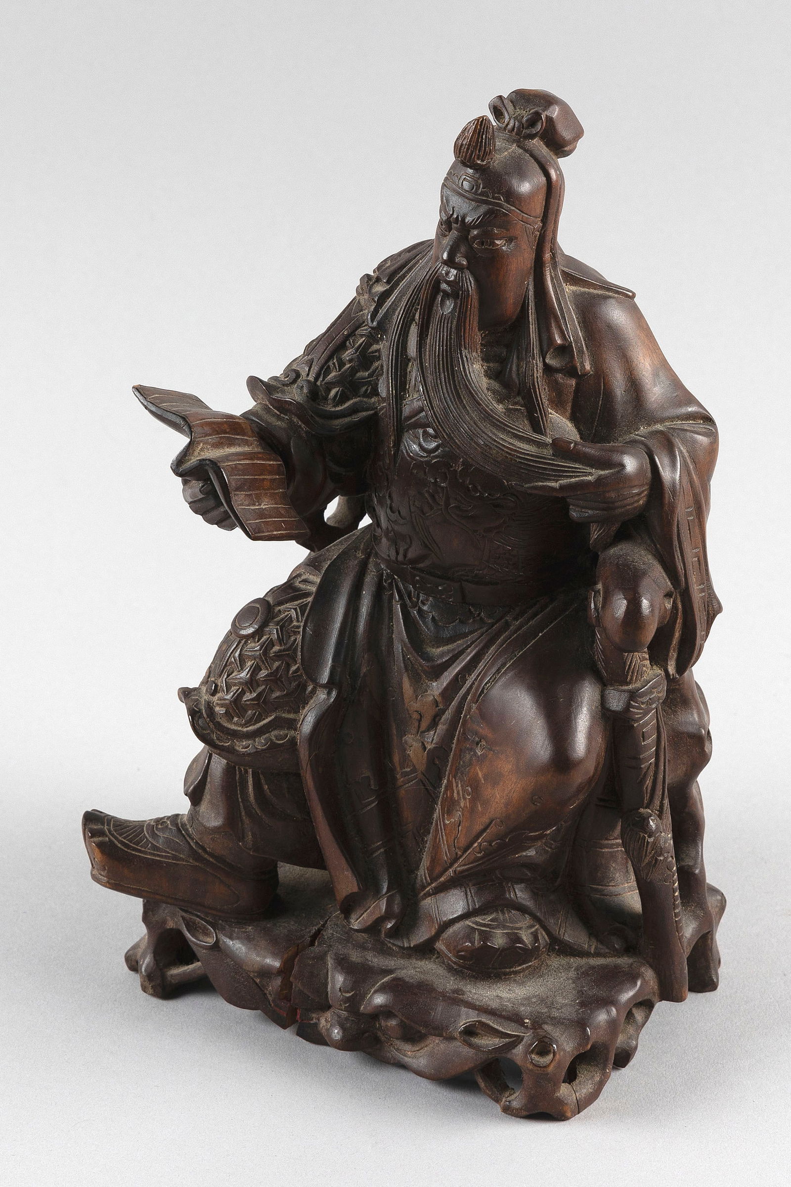 CHINESE CARVED WOOD FIGURE OF GUAN YU Late 19th/Early 20th Century Height 10.5".: CHINESE CARVED WOOD FIGURE OF GUAN YULate 19th/Early 20th CenturySeated on a chair atop a rockery base, holding a book in one hand and stroking his beard with the other.Height 10.5".