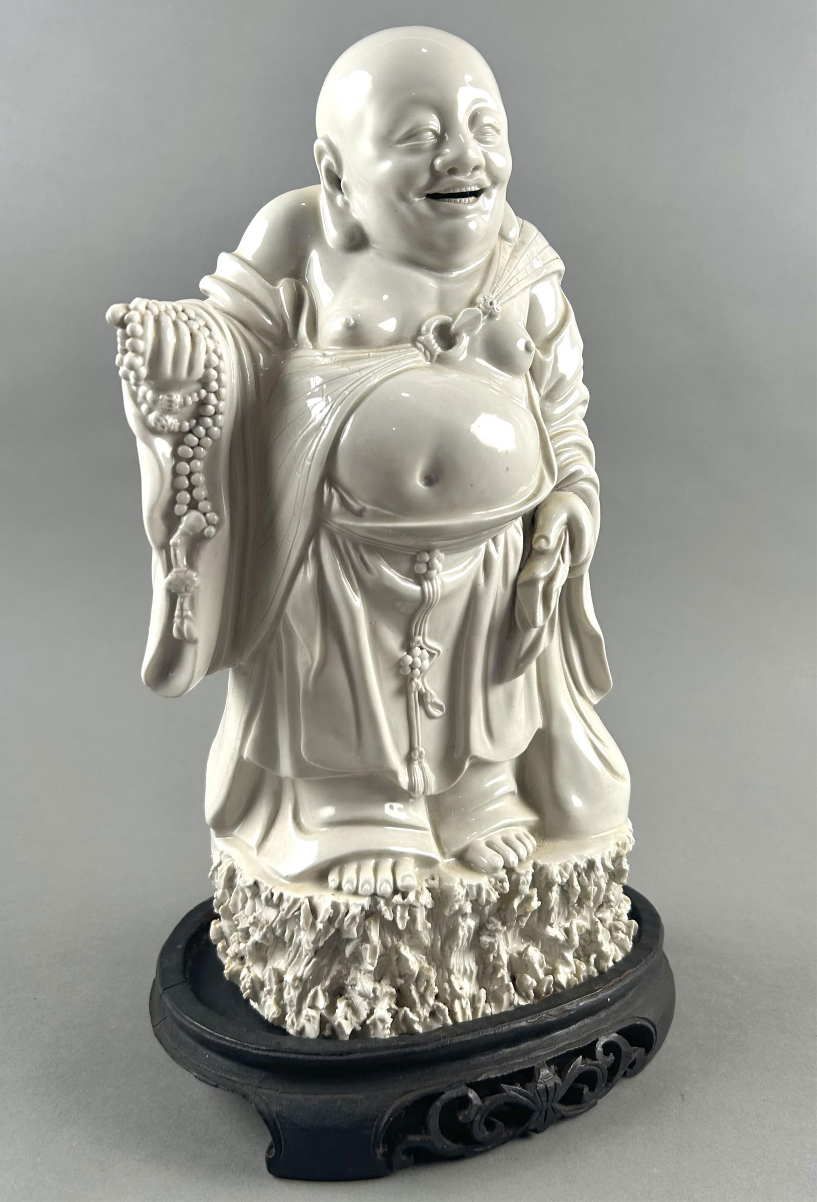 CHINESE BLANC DE CHINE PORCELAIN FIGURE OF BUDDHA Early 20th Century Height 12.5". Length 6". With a: CHINESE BLANC DE CHINE PORCELAIN FIGURE OF BUDDHAEarly 20th CenturyStanding on a conforming rockery base and holding prayer beads in his right hand.Height 12.5". Length 6". With a wooden stand, height