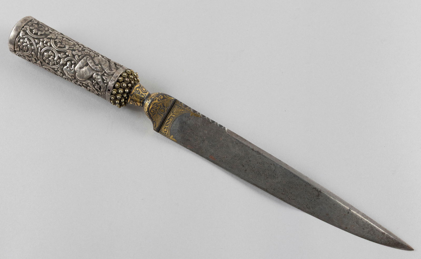 BURMESE DAGGER 1850s Total length 13". Length of blade 9".: BURMESE DAGGER1850sChased silver hilt with animal and foliate decoration. Damascus steel blade with gold inlay.Total length 13". Length of blade 9".