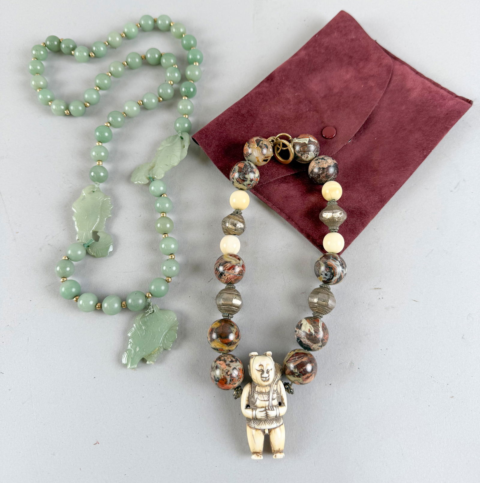 TWO CHINESE HARDSTONE NECKLACES Mid- to Late 20th Century Lengths 15" and 16".: TWO CHINESE HARDSTONE NECKLACESMid- to Late 20th CenturyStrand of celadon jade beads with three carved spacers, and a strand of puddingstone beads with a carved bone figural pendant. Gold-tone clasps