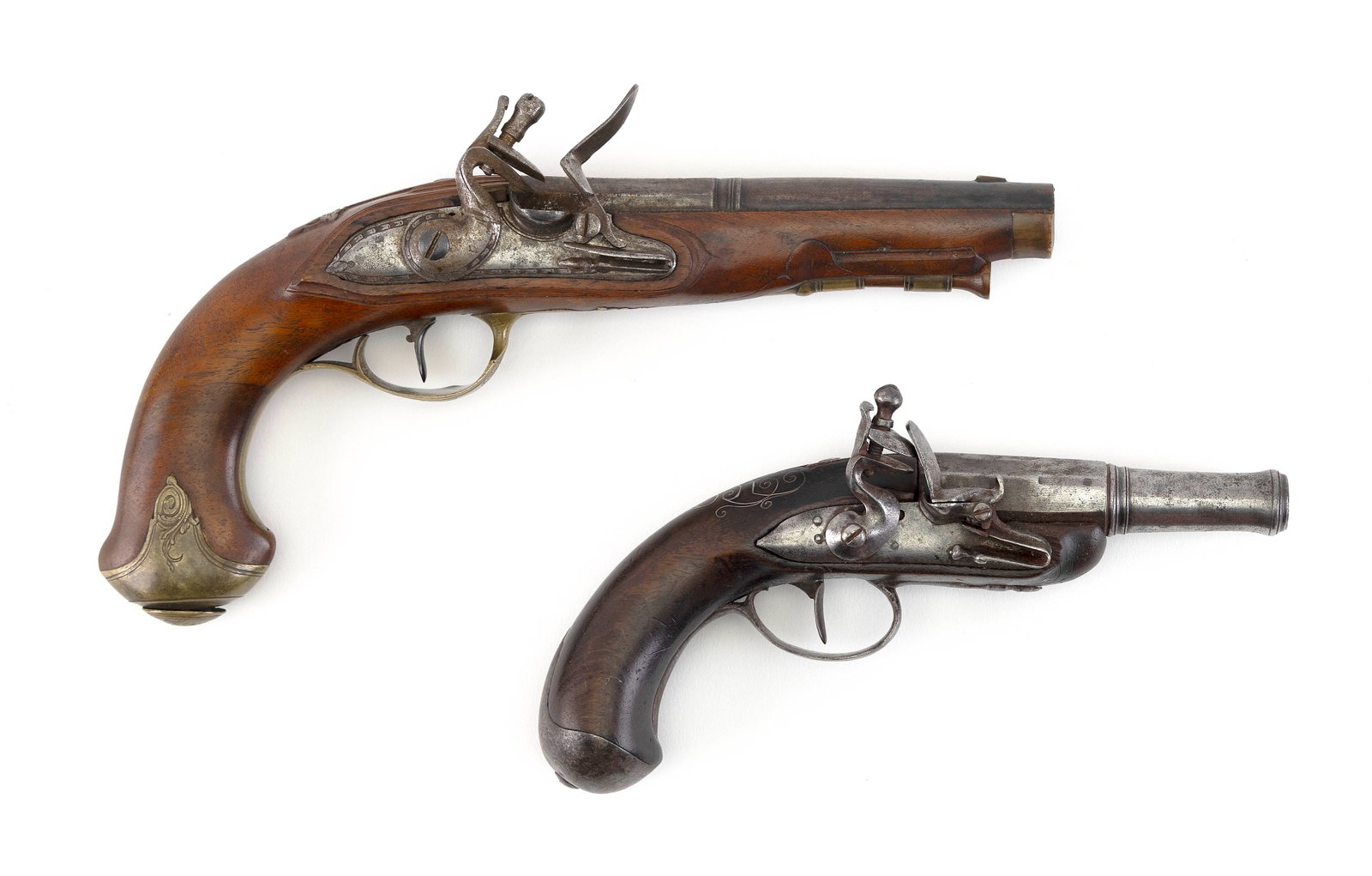 TWO FLINTLOCK PISTOLS Late 18th Century Length of barrels 4" and 5.5". Total lengths 8" and 10.5".: TWO FLINTLOCK PISTOLS Late 18th Century Approx. .31 cal. Both with part-octagonal, part-round barrels. One with inlaid silver wire scrolls. Other with raised carved leaves and engraved scrolls on the 