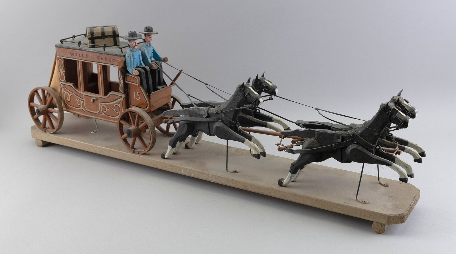 FOLK ART CARVING OF A WELLS FARGO STAGECOACH New Hampshire, Circa 1950 Height 34".: FOLK ART CARVING OF A WELLS FARGO STAGECOACH New Hampshire, Circa 1950 Team of four black and white painted horses draws a stagecoach being driven by two figures. Mounted on a white painted pine base.