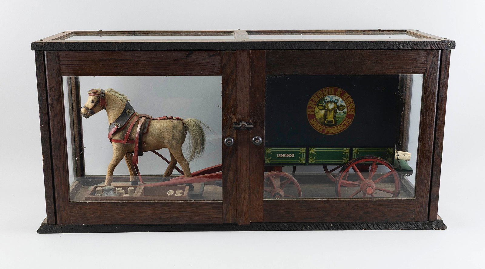 SCHOENHUT H.P. HOOD & SONS HORSE-DRAWN MILK WAGON PULL TOY Circa 1910 Case height 15". Length 30.5".: SCHOENHUT H.P. HOOD & SONS HORSE-DRAWN MILK WAGON PULL TOYCirca 1910Displayed in an oak glass case. Includes a delivery man, a case of milk bottles, a hide-covered horse on a wooden platform, and the