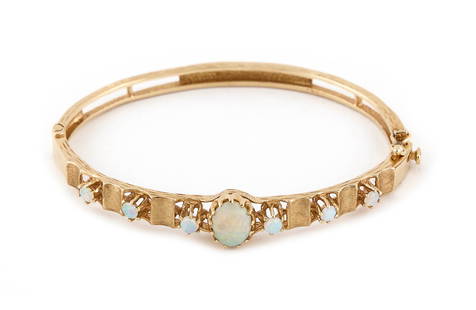14KT YELLOW GOLD AND OPAL BANGLE BRACELET Approx. 9.4 total dwt.: 14KT YELLOW GOLD AND OPAL BANGLE BRACELETOne approx. 7.0 x 9.0mm oval cabochon opal and six approx. 3.0mm round cabochon opals. Hinged with fold-over safety clasp. Width approx. 6.0mm. Length 7".Appro