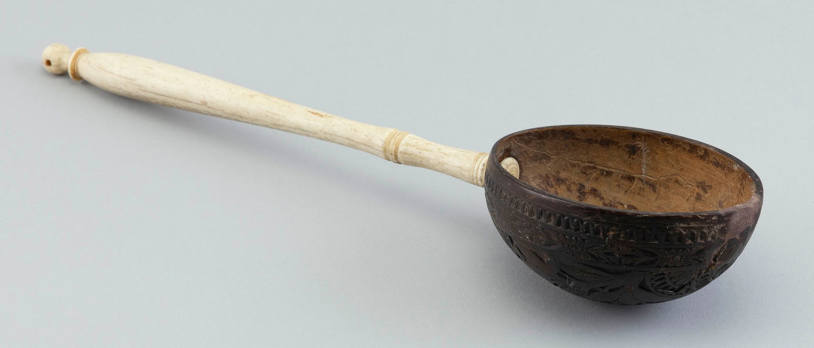 COCONUT SHELL DIPPER WITH WHALEBONE HANDLE 19th Century Length 12.75".: COCONUT SHELL DIPPER WITH WHALEBONE HANDLE19th CenturyCoconut shell carved with geometric, floral and foliate designs. Nicely turned handle.Length 12.75".