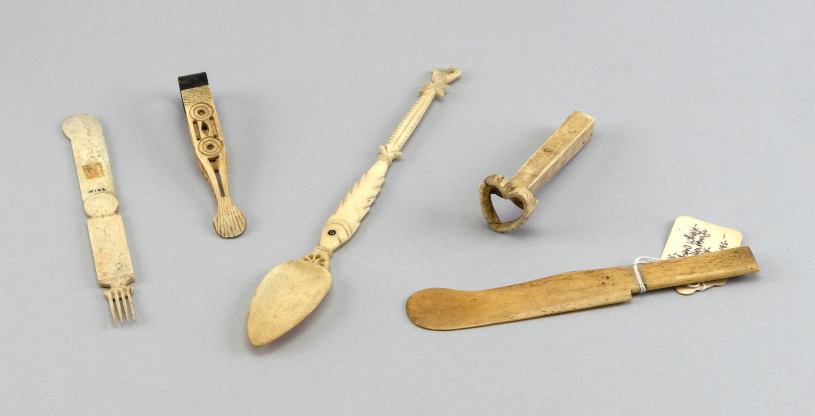 FIVE WHALEBONE KITCHEN ITEMS 19th Century Lengths from 3.5" to 9".: FIVE WHALEBONE KITCHEN ITEMS 19th Century A pair of sugar tongs, a heart-formed cookie press, a spoon with an elaborately carved fish-form handle and two butter knives, one with a delicate fork at the