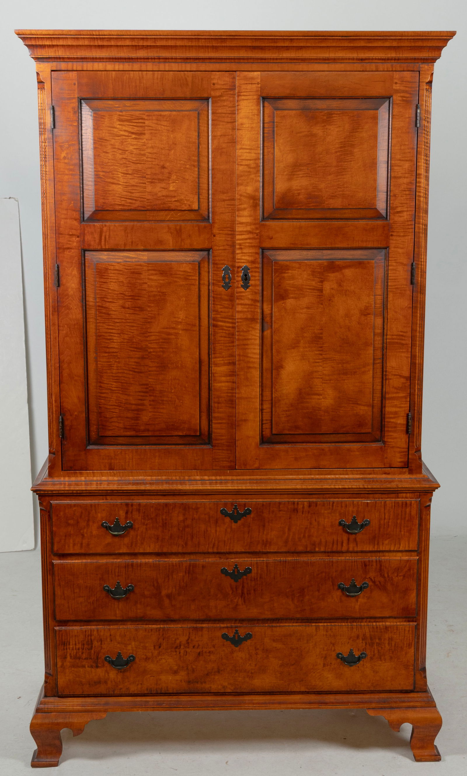 ELDRED WHEELER TIGER MAPLE TWO-PART LINEN PRESS Massachusetts, 20th Century Height 77". Width 43".: ELDRED WHEELER TIGER MAPLE TWO-PART LINEN PRESSMassachusetts, 20th CenturyUpper case with two paneled doors. Lower case with three full-width drawers and ogee feet. Labeled in one of the small drawers