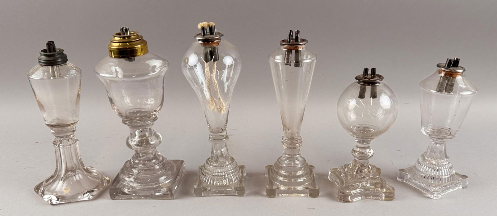 SIX CLEAR GLASS WHALE OIL LAMPS First Half of the 19th Century Heights from 7" to 8.5".: SIX CLEAR GLASS WHALE OIL LAMPSFirst Half of the 19th CenturyAll with free-blown fonts, pressed bases and original burners.Heights from 7" to 8.5". Provenance:William Dixon Collection.
