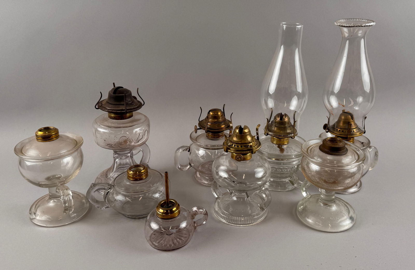 NINE CLEAR GLASS FLUID HAND LAMPS Late 19th/Early 20th Century Heights excluding chimneys from 3" to: NINE CLEAR GLASS FLUID HAND LAMPSLate 19th/Early 20th CenturyHeights excluding chimneys from 3" to 6". Provenance:William Dixon Collection.
