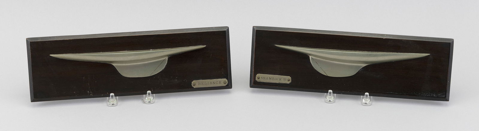 PAIR OF VICTOR METAL CO. MOUNTED HALF HULL YACHT MODELS Early 20th Century Lengths 11".: PAIR OF VICTOR METAL CO. MOUNTED HALF HULL YACHT MODELSEarly 20th CenturyThe Shamrock III and the Reliance. Mahogany backboards.Lengths 11".
