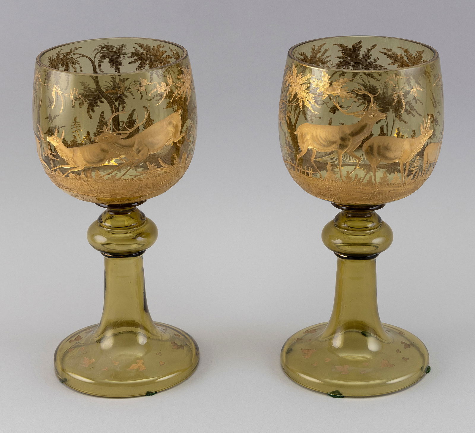 PAIR OF AMBER GLASS CHALICES WITH DECORATION OF DEER Germany/Bavaria, 19th Century Heights 10.75".: PAIR OF AMBER GLASS CHALICES WITH DECORATION OF DEERGermany/Bavaria, 19th CenturyEngraved and gilt painted scene of deer in a landscape encircles the bodies. Bases with small engraved and gilded flowe
