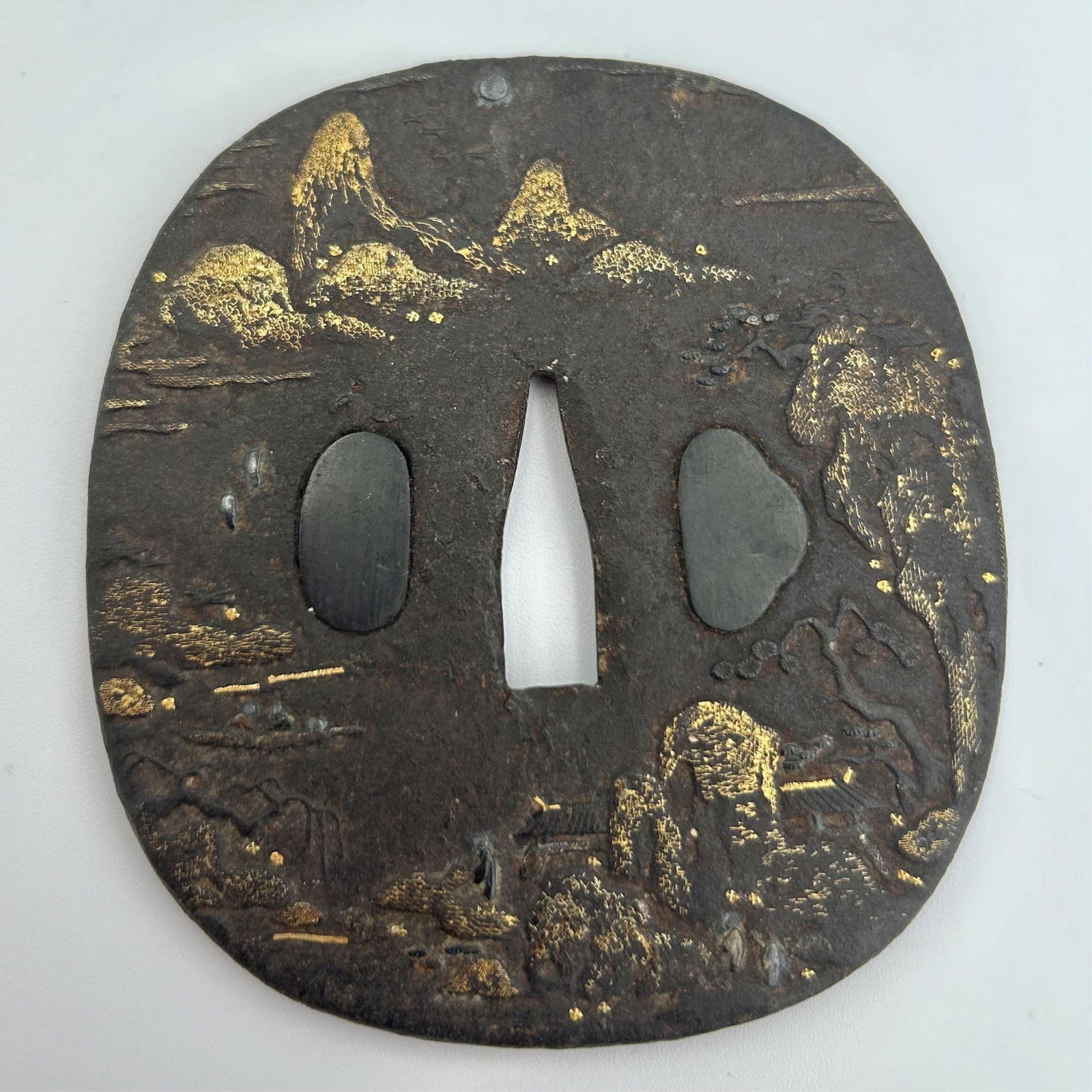 JAPANESE IRON NAGA MARU GATA TSUBA 18th/19th Century Length 3.25".: JAPANESE IRON NAGA MARU GATA TSUBA18th/19th CenturyRaised gilt mountainous landscape decoration.Length 3.25".