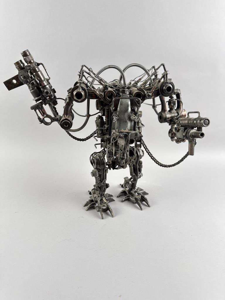 RECLAIMED ART SCULPTURE OF A GUN-TOTING PIVOTING ROBOT Contemporary Height 14.75". Width 16". Depth: RECLAIMED ART SCULPTURE OF A GUN-TOTING PIVOTING ROBOTContemporaryMade of various welded car parts.Height 14.75". Width 16". Depth 9".
