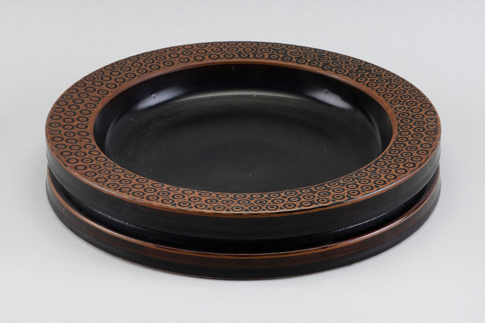 STIG LINDBERG (SWEDEN, 1916-1982) FOR GUSTAVSBERG STONEWARE SHALLOW BOWL Sweden, Mid-20th Century: STIG LINDBERG (SWEDEN, 1916-1982) FOR GUSTAVSBERG STONEWARE SHALLOW BOWLSweden, Mid-20th CenturyBrown and black glaze with impressed fish eye decoration about the rim. Incised "Stig L" signature on un
