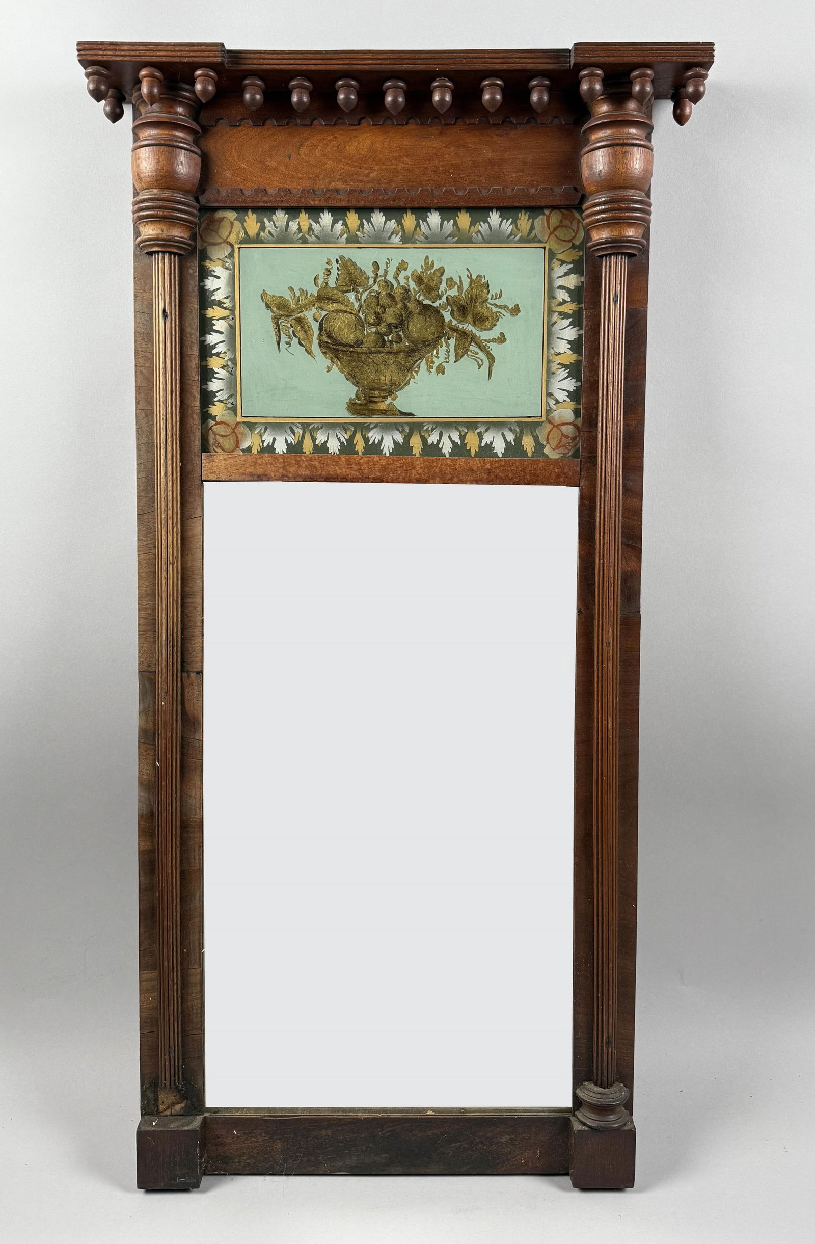 FEDERAL TABERNACLE MIRROR WITH EGLOMISE PANEL 19th Century Height 40.5". Width 21". Depth 3".: FEDERAL TABERNACLE MIRROR WITH EGLOMISE PANEL19th CenturyMolded cornice with acorn drops. Upper reverse-painted panel depicts a fruit basket and an oak leaf and floral border. Slender fluted side colu