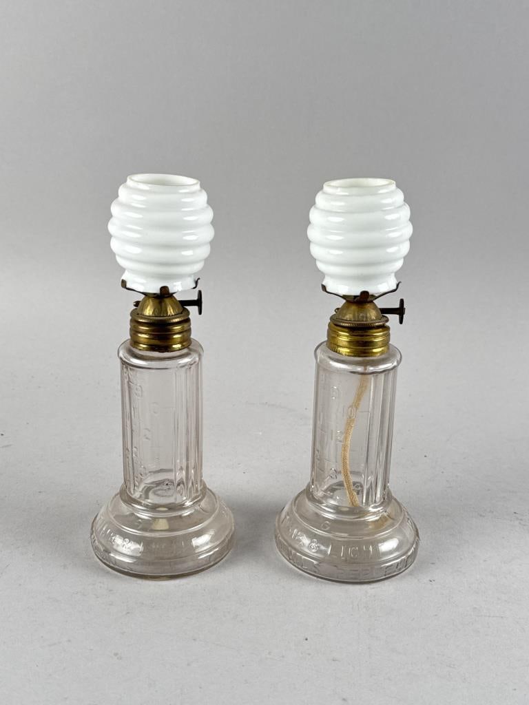 TWO TIME INDICATING LAMPS Fourth Quarter of the 19th Century Heights to top of burners 5.25".: TWO TIME INDICATING LAMPSFourth Quarter of the 19th CenturyClear glass column-form reservoirs with molded scales to indicate the time elapsed since the lamp was lit. Marked "Pride of America Time & Li