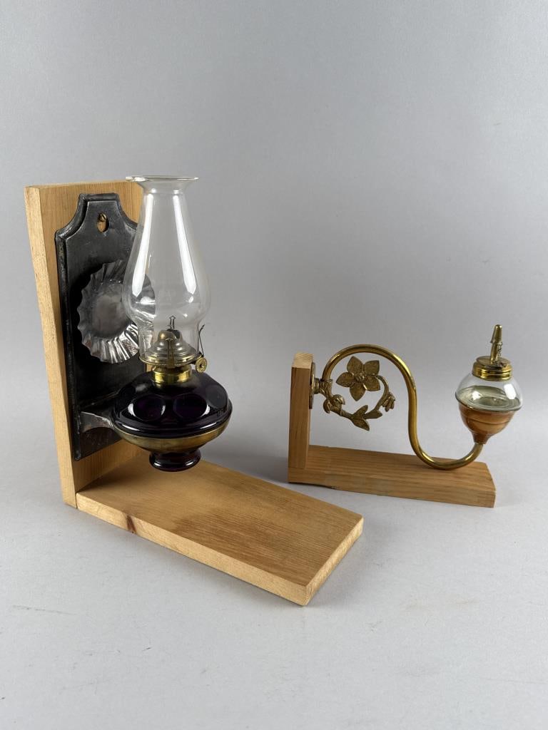 TWO OIL WALL SCONCES 19th Century: TWO OIL WALL SCONCES19th Century1) Metal back plate and crimped reflector, probably tin. Amethyst glass reservoir. Height 10.5". Width 4.5". Depth 5". Mounted on a wooden stand. 2) Brass scrolled arm