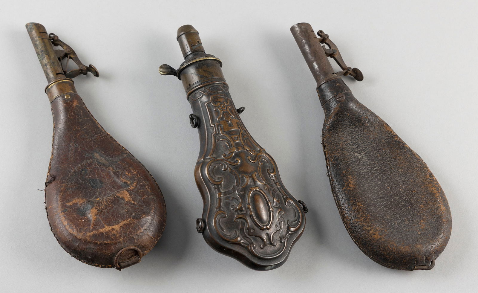 THREE POWDER FLASKS 19th Century Lengths from 8" to 9".: THREE POWDER FLASKS19th CenturyTwo leather and one copper.Lengths from 8" to 9".