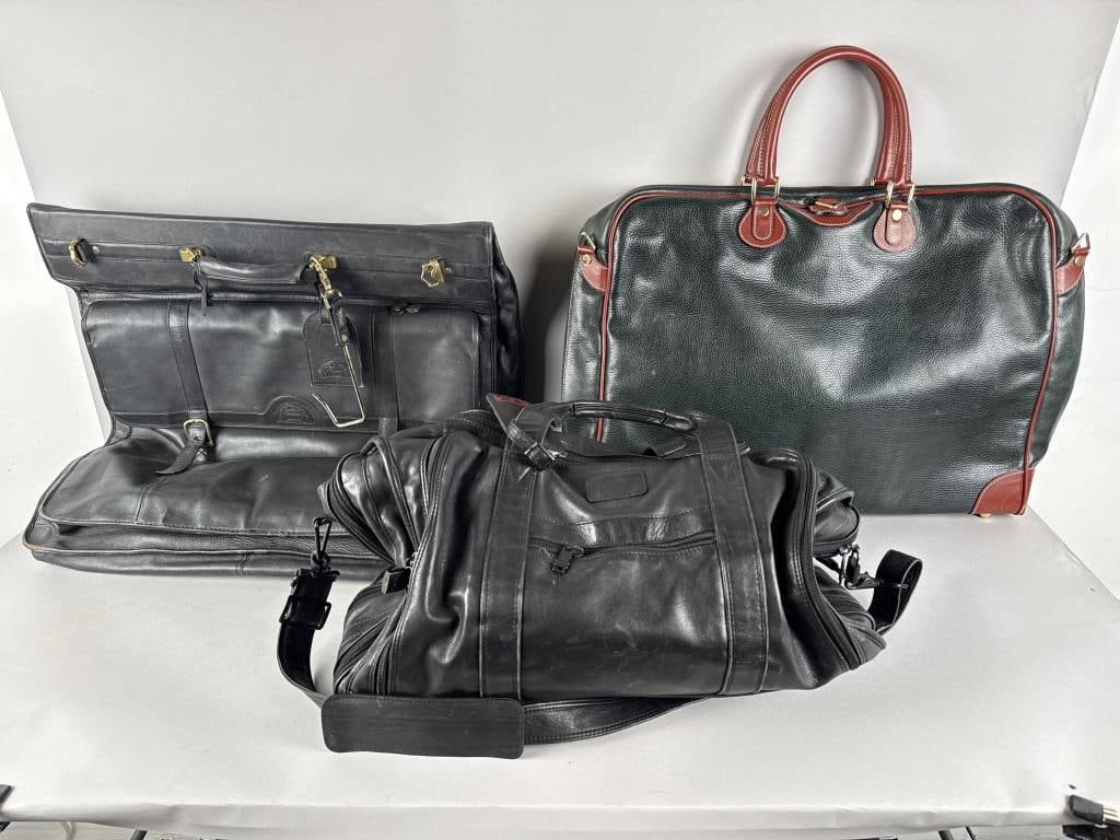 THREE LEATHER TRAVEL BAGS America, 21st Century: THREE LEATHER TRAVEL BAGSAmerica, 21st Century1) LAND black garment bag with gold-tone hardware. 23" x 23".2) Cole Haan forest green garment bag with russet brown detailing and gold-tone hardware. 19"