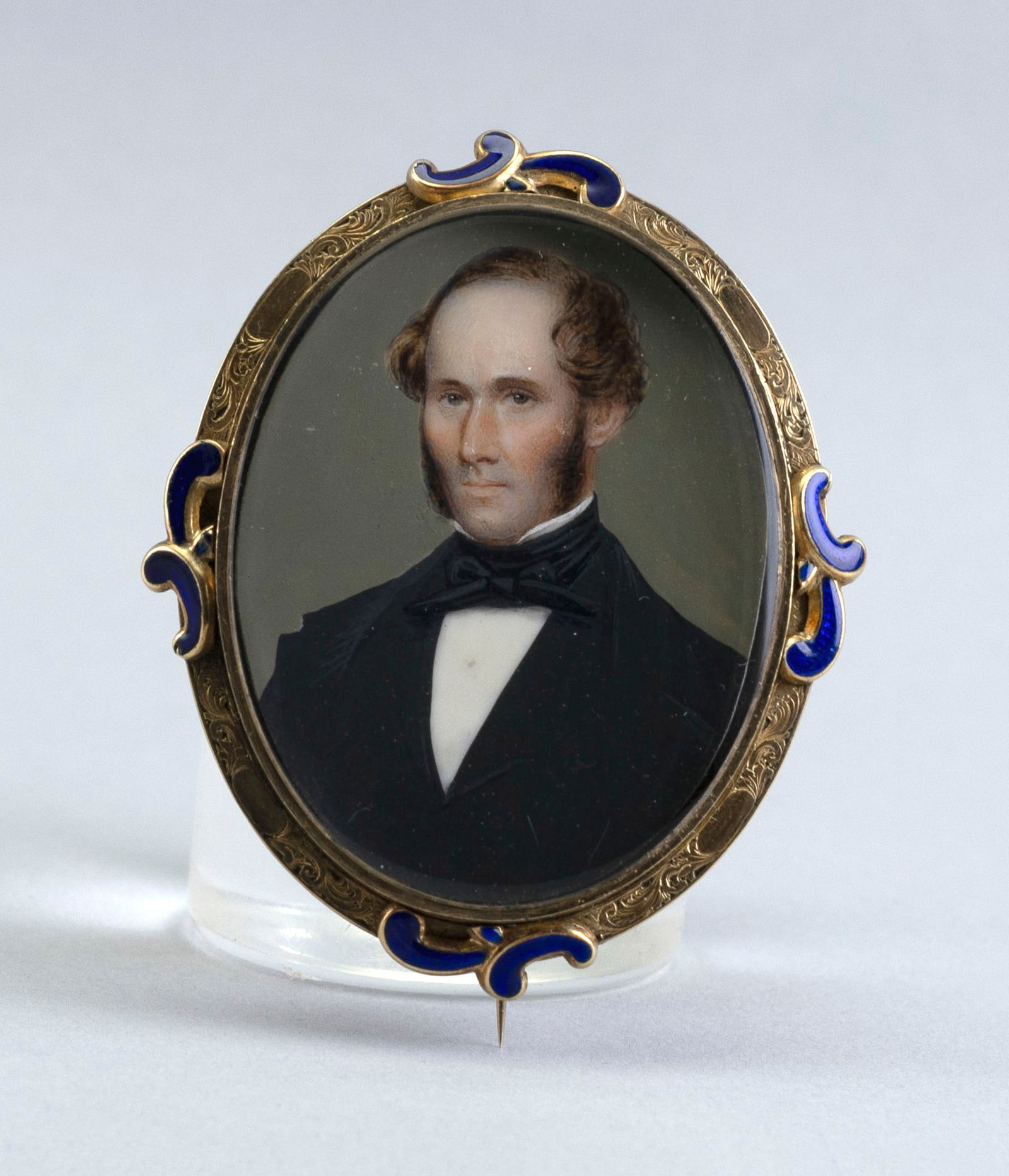 PORTRAIT MINIATURE OF A GENTLEMAN SET WITHIN A GOLD BROOCH Scotland, Mid-19th Century Approx. 18.94: PORTRAIT MINIATURE OF A GENTLEMAN SET WITHIN A GOLD BROOCHScotland, Mid-19th CenturyPainted on ivory. Artist identified on reverse as Hor. Nelson, a Benezet listed artist. Cobalt blue enameled gold br