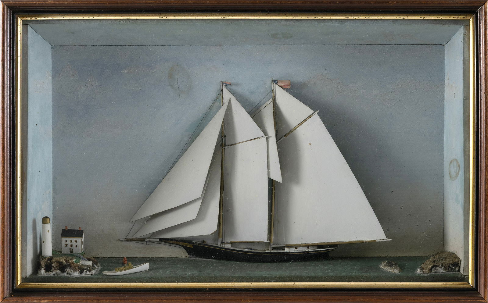 MARITIME DIORAMA WITH LIGHTHOUSE Late 19th Century Case height 19". Width 30.5". Depth 5".: MARITIME DIORAMA WITH LIGHTHOUSELate 19th CenturyDepicts a two-masted schooner flying an American flag off an island lighthouse. Painted sky background. Housed in a shadow box case.Case height 19". Wi