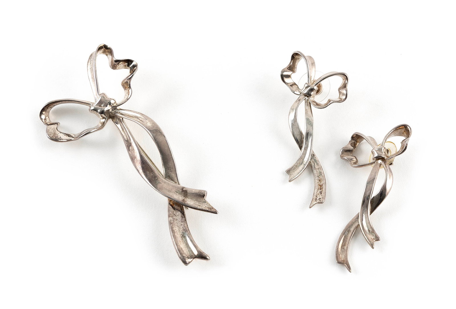 TIFFANY & CO. STERLING SILVER BOW PIN AND PAIR OF MATCHING EARRINGS Approx. 21.5 total dwt.: TIFFANY & CO. STERLING SILVER BOW PIN AND PAIR OF MATCHING EARRINGS1) Bow pin. Approx. 1.625" x 3.625".2-3) Pair of earrings. Lower section moveable. Approx. 1" x 2.25".Each stamped.Approx. 21.5 total