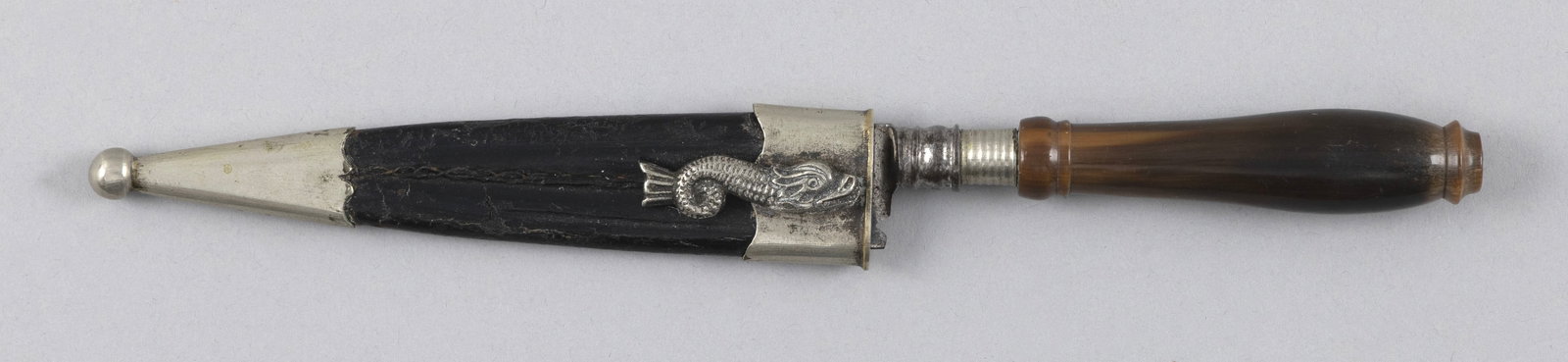 DIMINUTIVE DAGGER WITH SHEATH 19th Century Length 8.25".: DIMINUTIVE DAGGER WITH SHEATH 19th Century Marked on blade "Primeira [...]". Leather and metal sheath with a dolphin figure applied to one side. Length 8.25".