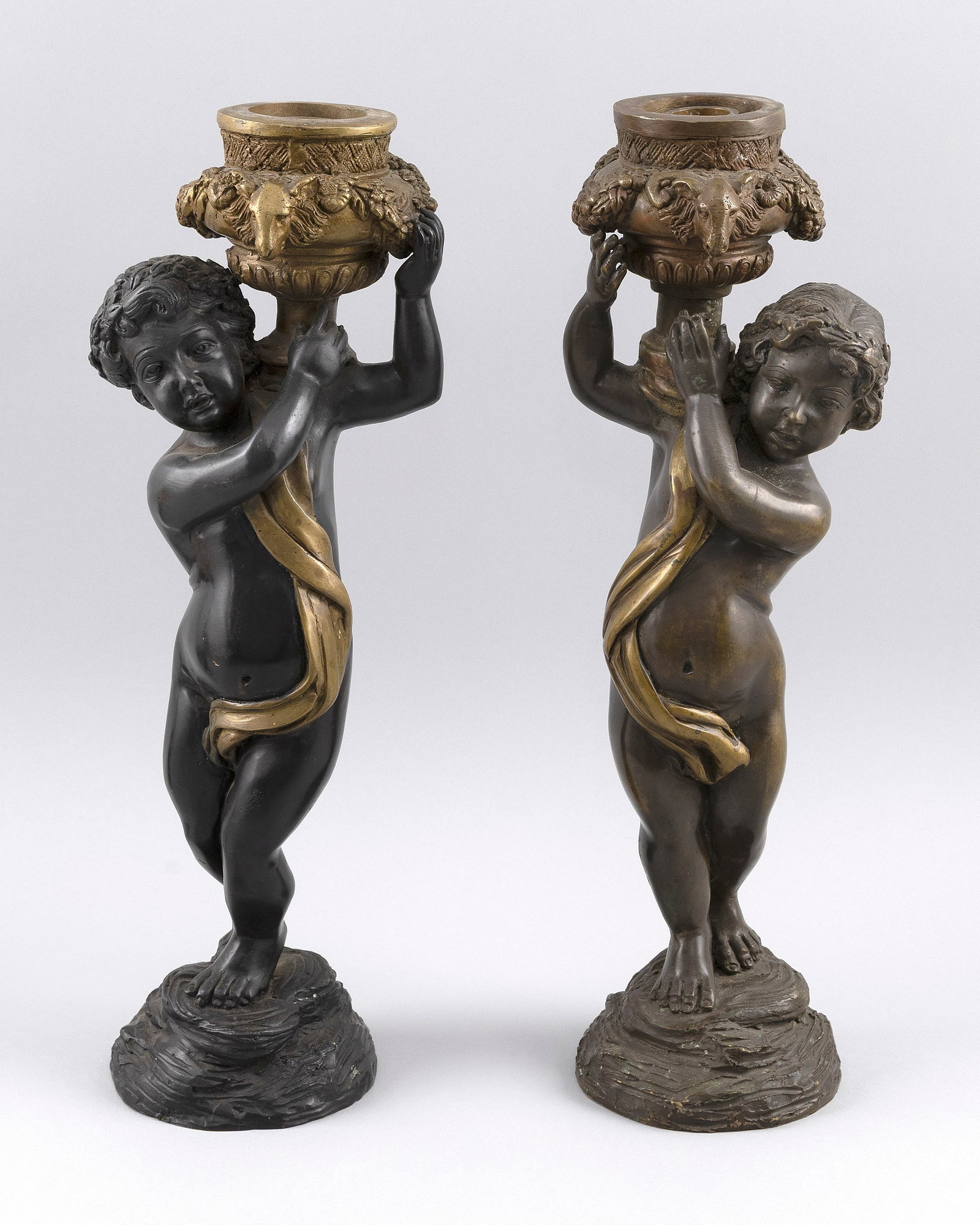 PAIR OF FRENCH BRONZE PUTTI CANDLE HOLDERS 19th Century: PAIR OF FRENCH BRONZE PUTTI CANDLE HOLDERS 19th Century Putti hold aloft candle cups adorned with ram's heads.
