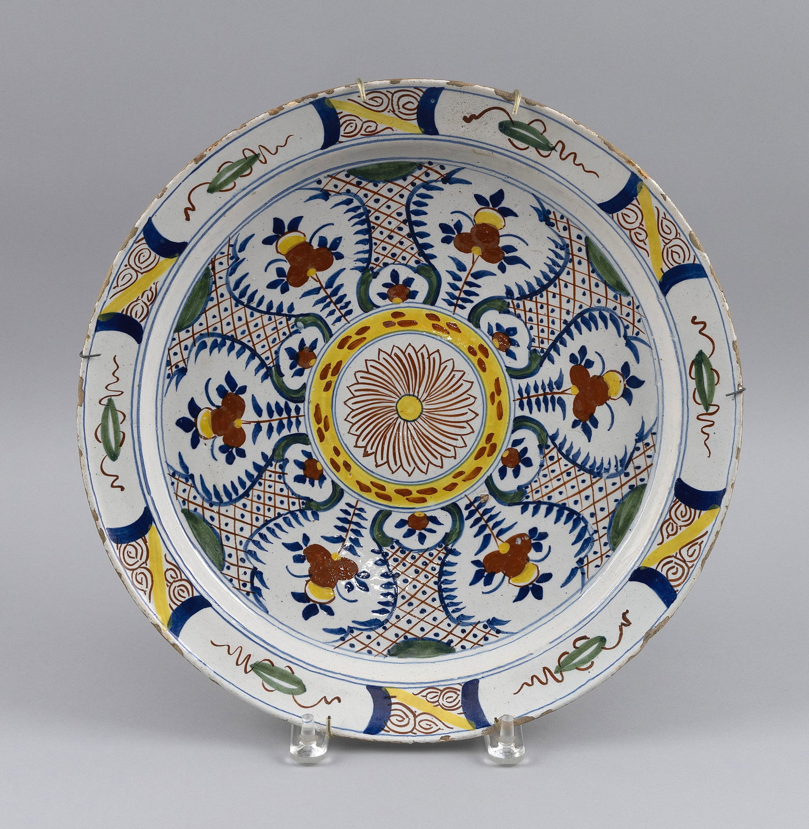 DUTCH POLYCHROME TIN-GLAZED CHARGER 18th Century Diameter 14".: DUTCH POLYCHROME TIN-GLAZED CHARGER 18th Century Decoration of a central blossom surrounded by floral sprigs and lattice panels in yellow, rust, green and blue. Diameter 14".