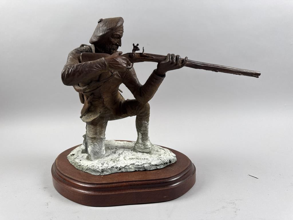 HARTMANN BRONZE SCULPTURE OF A FRONTIERSMAN Height 15". Length 22". Width 11".: HARTMANN BRONZE SCULPTURE OF A FRONTIERSMAN Crouching in the snow and aiming his longarm, with snowshoes strapped to his back and a powderhorn, canteen, knife and ax strapped to his belt. Signed and n