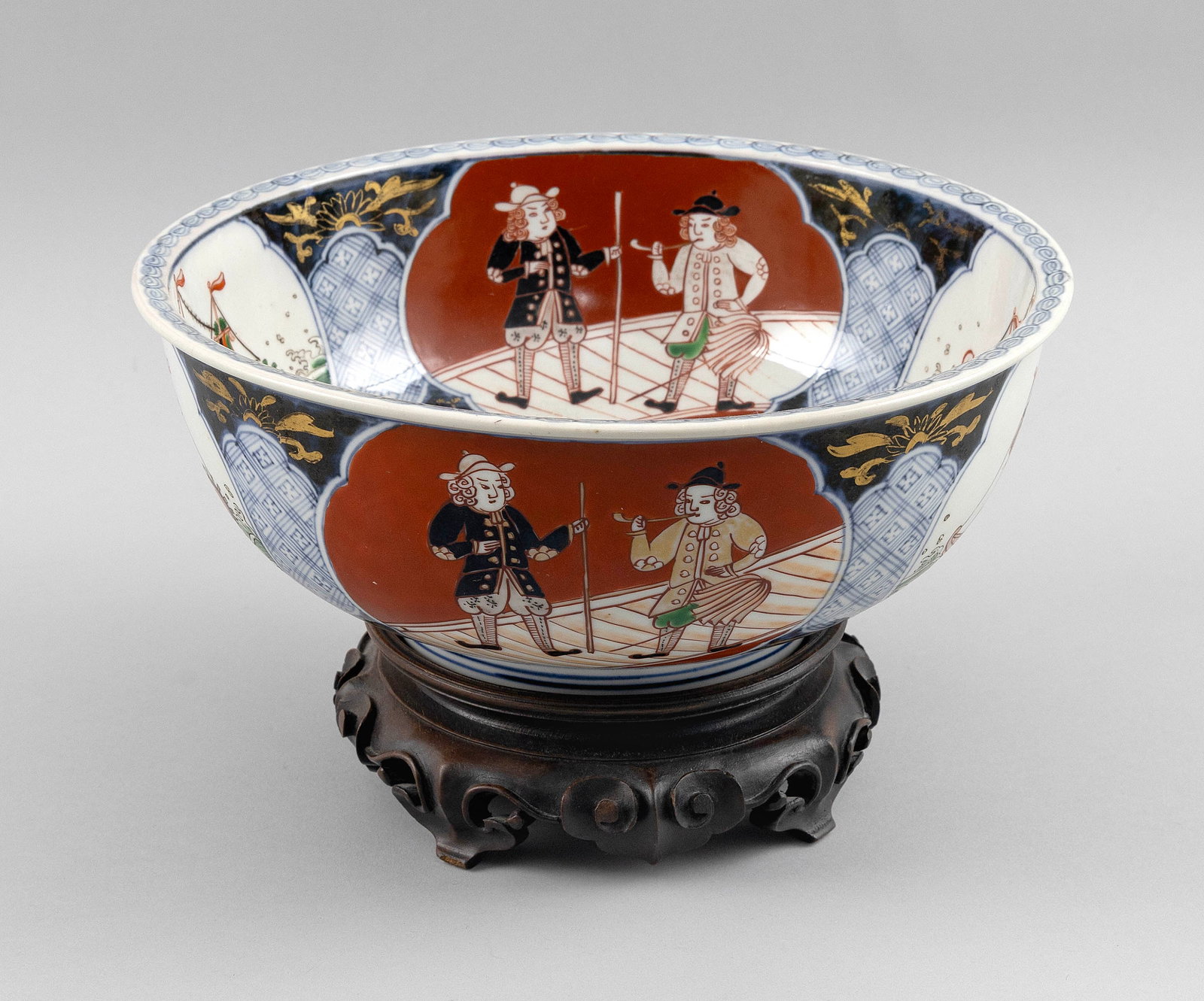 JAPANESE IMARI PORCELAIN BOWL Late 19th/Early 20th Century Height 4". Diameter 10". With carved wood: JAPANESE IMARI PORCELAIN BOWL Late 19th/Early 20th Century Exterior and interior with alternating decoration of ships and Western figural vignettes. Height 4". Diameter 10". With carved wood stand. Pr