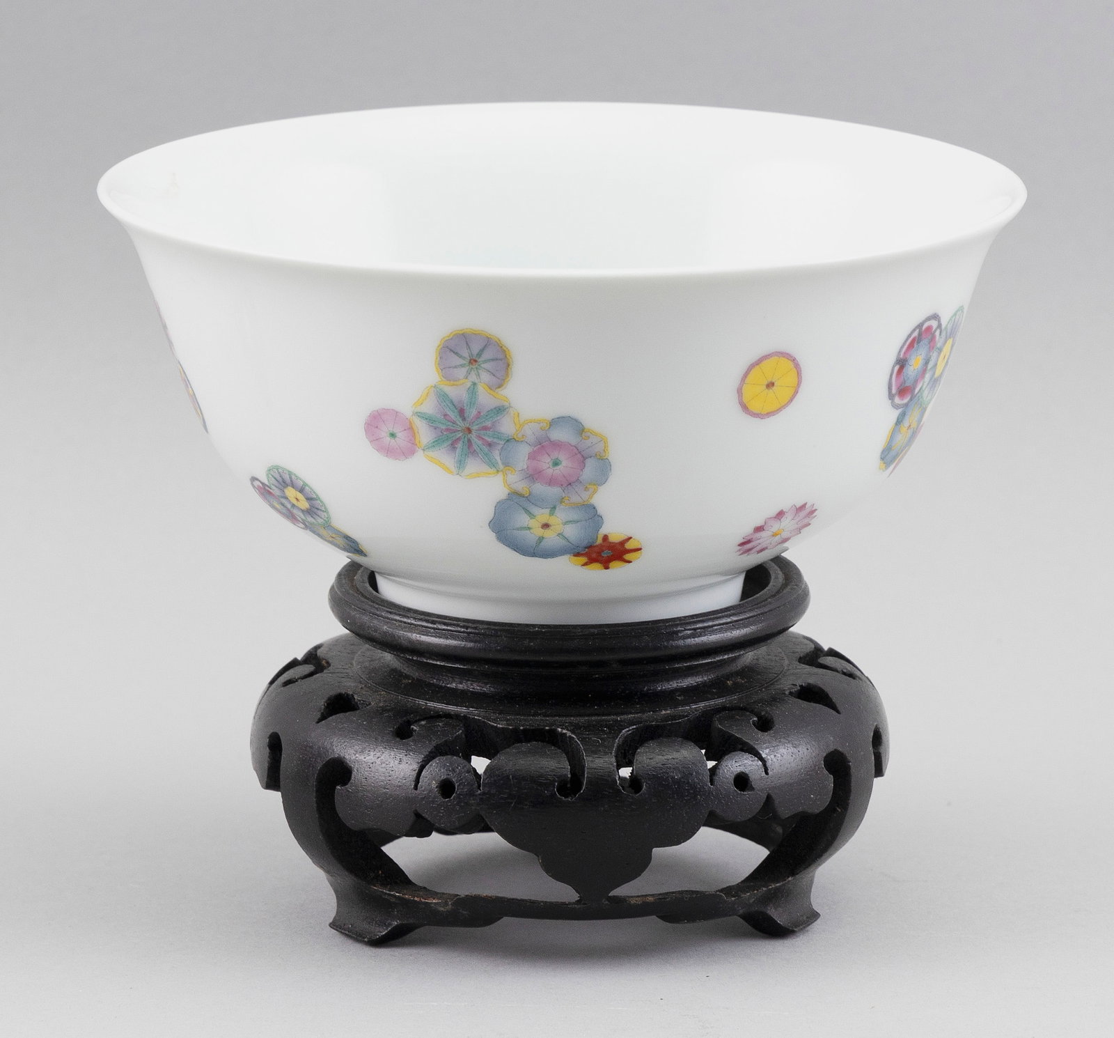 CHINESE FAMILLE ROSE PORCELAIN BOWL Early 20th Century Height 3". Diameter 6". With wood stand.: CHINESE FAMILLE ROSE PORCELAIN BOWL Early 20th Century Scattered clusters of floral rondels against a white ground. Four-character Qianlong mark on base. Height 3". Diameter 6". With wood stand.