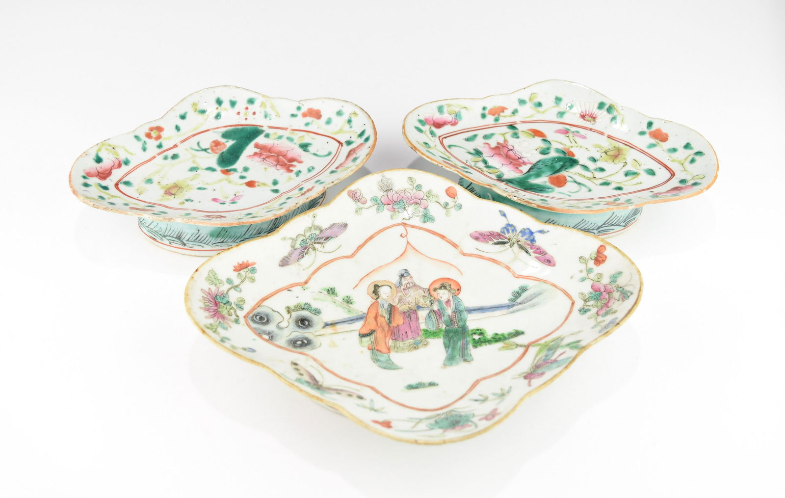 THREE 19TH CENTURY CHINESE FAMILLE ROSE FRUIT PLATES: With scalloped rim, all decorated with flowers, fruits, bats and waves, the larger one also decorated with a figural scene of the Trio of Feng Chen San Xia at the center. All have glaze flakes at the