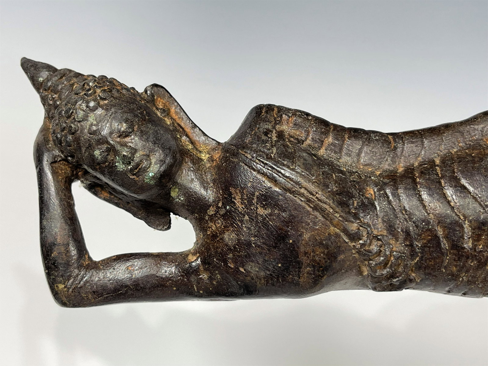 AN ANTIQUE SOUTH ASIAN CAST BRONZE RECLINING BUDDHA: It depicts Buddha in the last stage of illness. 19th century or older. Good condition. Size: 28 CM L; 7 CM H