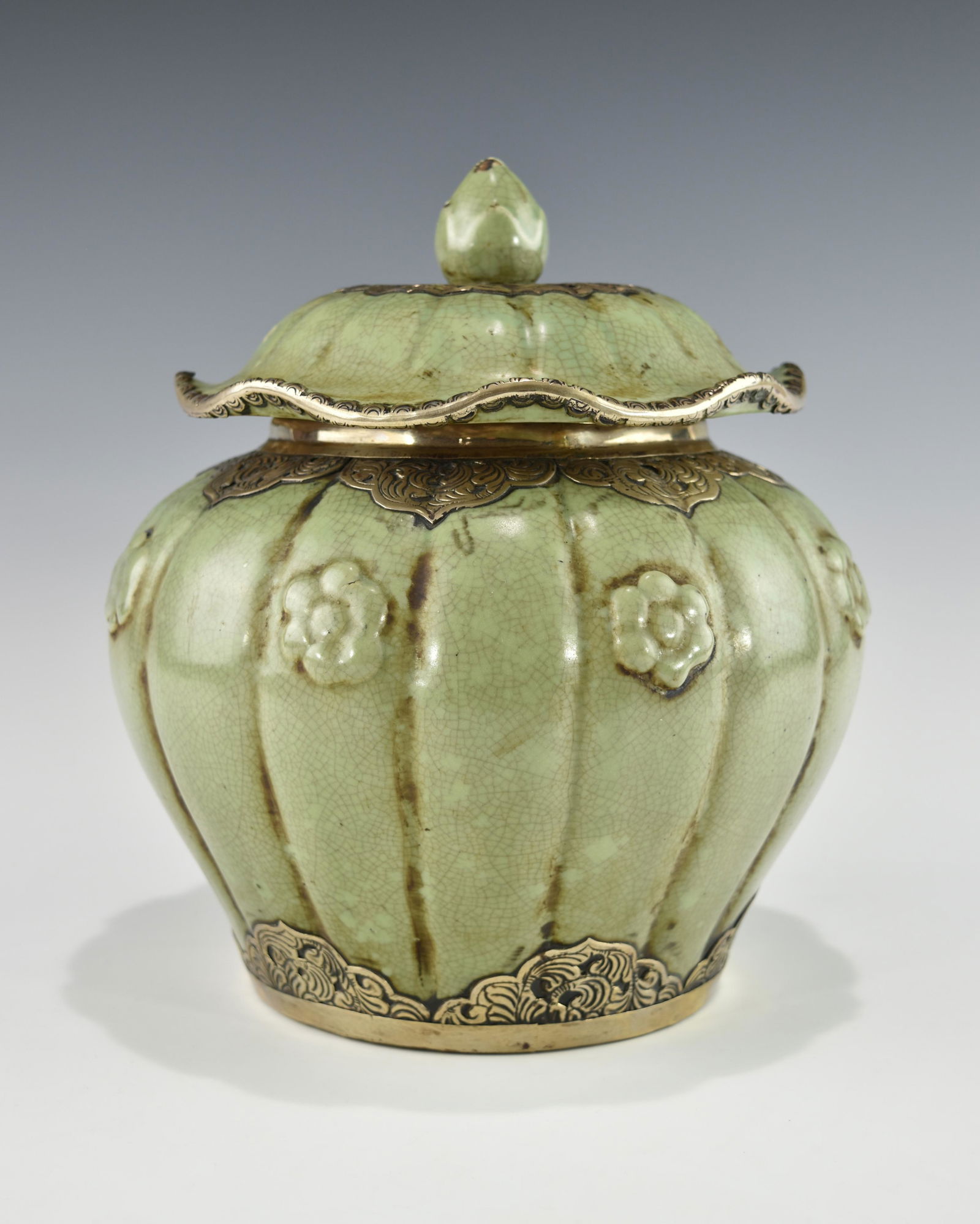 A CHINESE CELADON LOBED BALUSTER JAR WITH LOTUS LEAF LID: Possibly 19TH century or older. The lobed blauster jar is adorned with prunus flowers in high relief. The celadon glazed surface is suffuzed with glaze craquelure both on the lid and the exterior of t